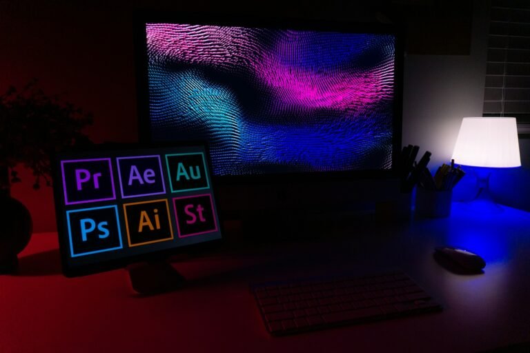 A computer and tablet glowing with colorful graphics in a dark workspace