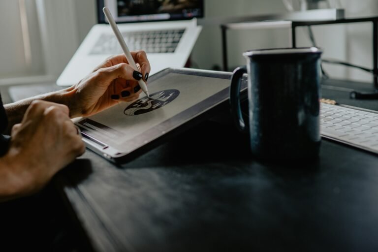 A person drawing on a tablet with a white stylus beside a dark mug and keyboard