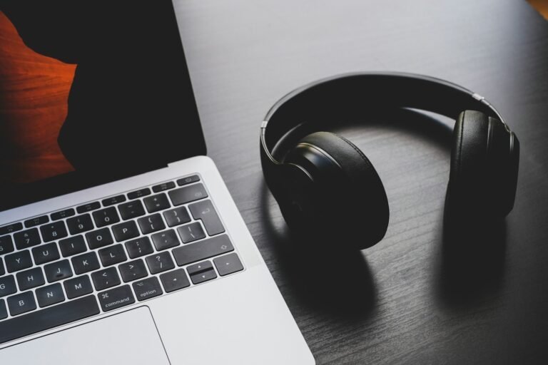 Black over-ear headphones resting on a desk beside a silver laptop
